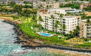 A coastal hotel with multiple floors, a swimming pool, and palm trees. - Experience Oceanfront Grandeur: Royal Mauian #418 - Spectacular Views Await! (Kihei, Maui)