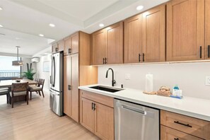 A modern kitchen with wooden cabinets, stainless steel appliances, and a white countertop. - Experience Oceanfront Grandeur: Royal Mauian #418 - Spectacular Views Await! (Kihei, Maui)