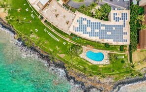 An aerial view of a resort with a swimming pool, a covered area with solar panels, and a beachside location. - Experience Oceanfront Grandeur: Royal Mauian #418 - Spectacular Views Await! (Kihei, Maui)