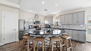 A modern kitchen with a central island, bar stools, stainless steel appliances, and a herringbone tile backsplash. - Front Row | Pet-Friendly, Stunning Beach Views (Galveston)
