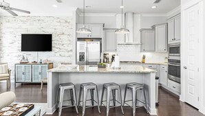 A modern kitchen with white cabinetry, a large island with stools, stainless steel appliances, and a rustic brick accent wall. - "Lucky Old Sun" - Prominence - 3BR / 2.5 BA - Sleeps 9 - 6 Passenger Golf Cart (Santa Rosa Beach)