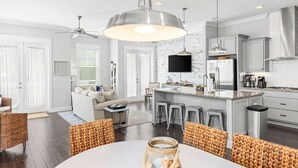 A modern kitchen with a central island, bar stools, and a dining area with a round table. - "Lucky Old Sun" - Prominence - 3BR / 2.5 BA - Sleeps 9 - 6 Passenger Golf Cart (Santa Rosa Beach)