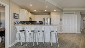 A modern kitchen with white bar stools, a stainless steel refrigerator, and a built-in oven. - 2415 SeaCrest-WOW Views!  You can't beat these oceanviews. (Hilton Head Island)