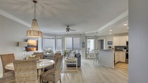 A spacious living area with a dining table, wicker chairs, a large window, and a kitchen with white cabinets and a microwave. - 2415 SeaCrest-WOW Views!  You can't beat these oceanviews. (Hilton Head Island)