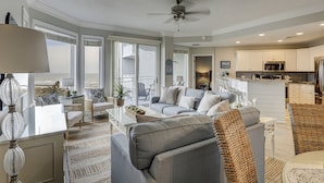 A spacious living room with a gray sofa, a coffee table, and a dining area with a white table. There is a kitchen with white cabinets and a stainless steel refrigerator. - 2415 SeaCrest-WOW Views!  You can't beat these oceanviews. (Hilton Head Island)
