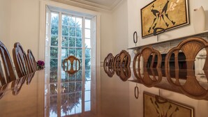 A dining area with a long wooden table and chairs, a large window with a view of trees, and wall-mounted artwork. - The Patrick Kavanagh Suite - hiphipstay (Dublin)