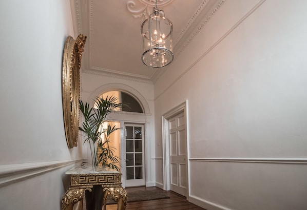 A hallway with a marble console table, a potted plant, a mirror, and a door leading to another room.