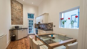 A modern kitchen with a brick wall, white cabinets, and a dining area with a glass table. - The Patrick Kavanagh Suite - hiphipstay (Dublin)