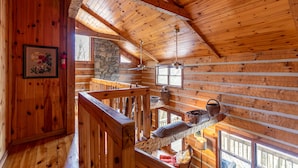 L’intérieur d’un chalet en bois comprend une chambre à coucher située en mezzanine, un mur en pierre, des poutres en bois et une cheminée.
