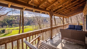 Une terrasse en bois avec un canapé en osier et une vue sur une vallée verdoyante.