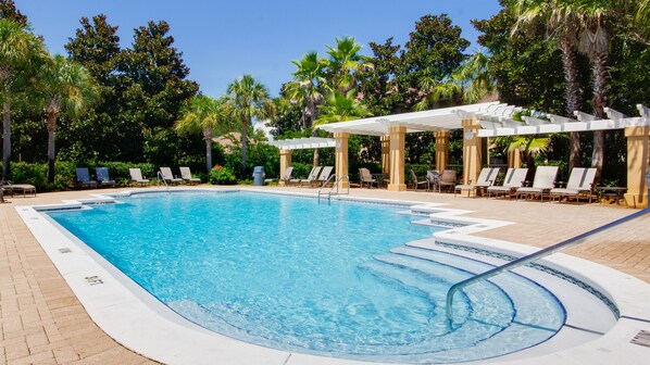 A rectangular swimming pool with clear blue water, surrounded by lounge chairs and palm trees.