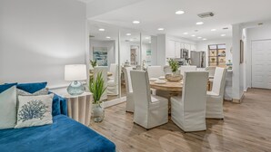 Un soggiorno moderno con un divano blu, una zona pranzo con sedie bianche e una cucina sullo sfondo.