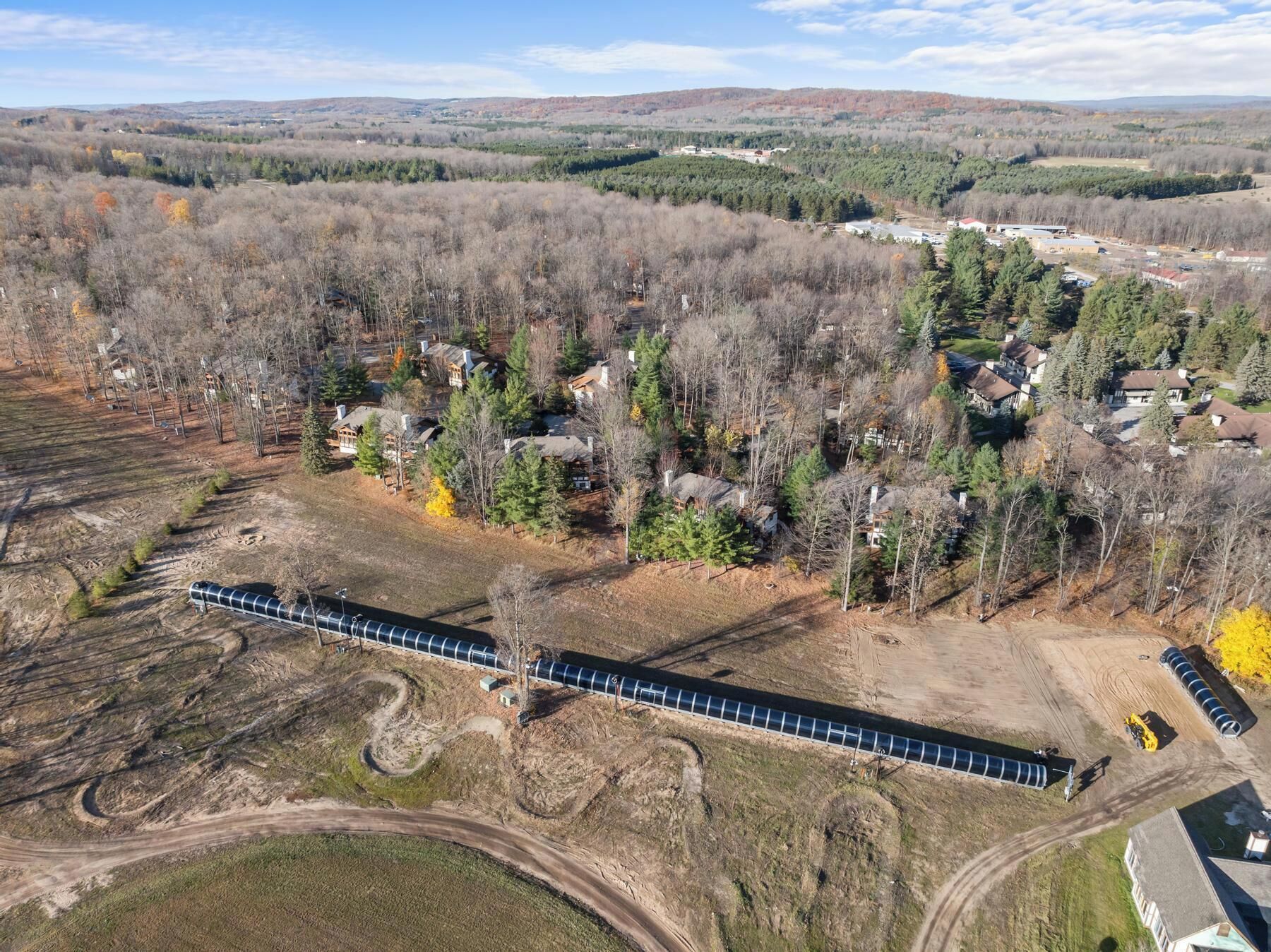 Luchtbeeld van een woongebied met huizen, een treinspoor en omliggende beboste heuvels.