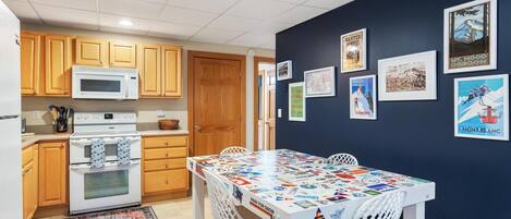 A compact kitchen with wooden cabinets, a microwave, an oven, and a dining table with a colorful placemat.