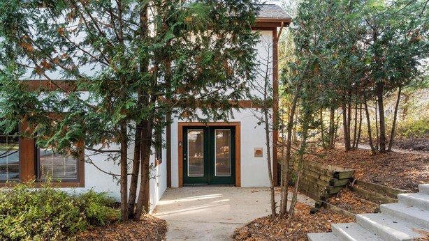 A modern building with a green door, a wooden porch, and a concrete pathway leading to a set of steps.