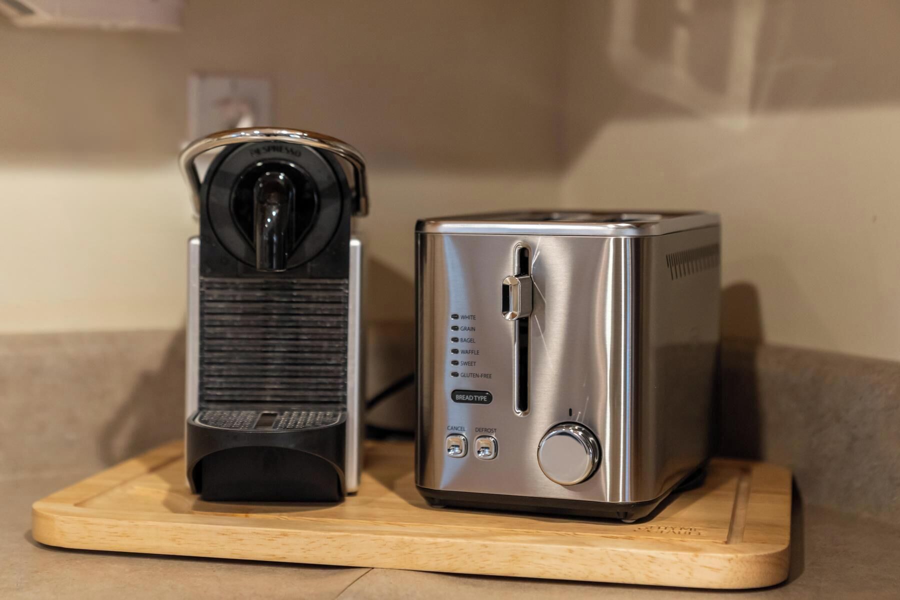 Un grille-pain en acier inoxydable et une cafetière noire, posés sur une planche en bois.