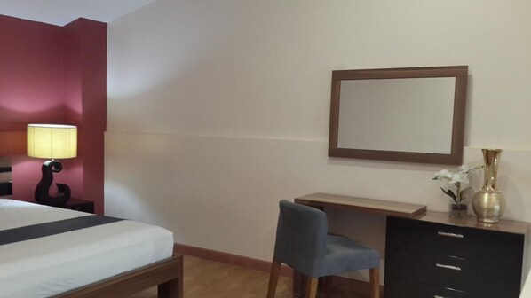 A hotel room with a bed, desk, chair, dresser, lamp, mirror, and a vase with flowers. - Ybc Grand Hotel (Olongapo)