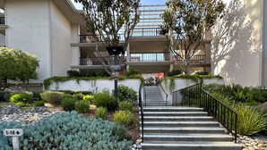 Un edificio de varios pisos con una escalera central, rodeado de jardines ajardinados y una variedad de plantas.
