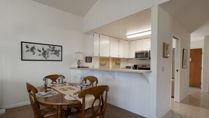Un comedor con una mesa y sillas de madera, una cocina con armarios blancos y un microondas, y una obra de arte enmarcada en la pared.