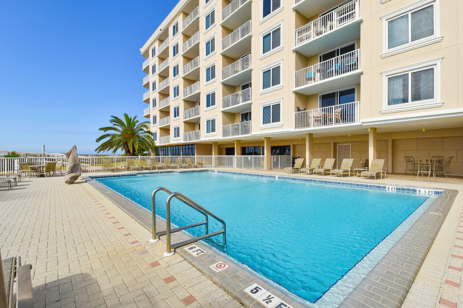 A swimming pool with a lifeguard stand, lounge chairs, and a multi-story building with balconies.