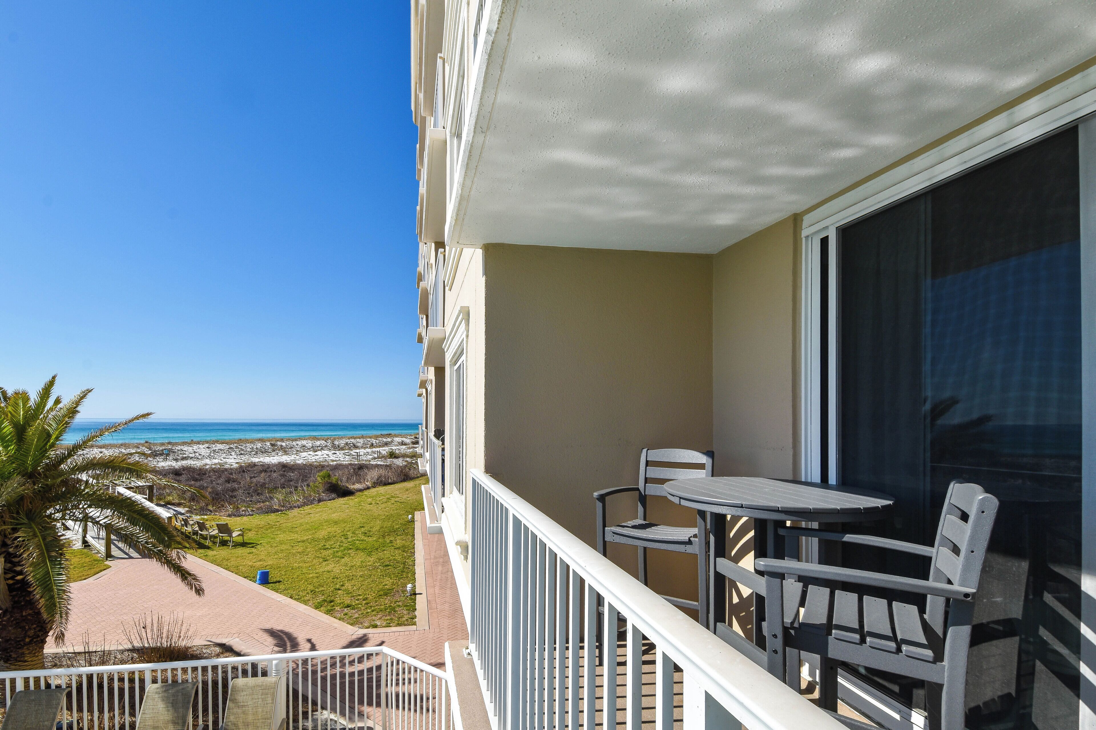 A balcony with a table and chairs, overlooking a beach and ocean.