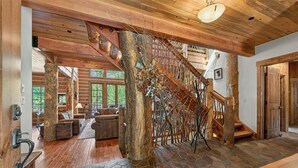 A wooden interior with a stone floor, a staircase with a wooden railing, and a view of the outdoors. - Bullshead By Tahoe Getaways - 4700SQ FT Luxury Riverfront Estate w Hot Tub (Olympic Valley)