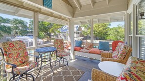 A covered patio with wicker furniture, a small table, and a bench with colorful cushions. - Family-Friendly 4BR Cottage with Pool View - Hidden Dunes Resort (Miramar Beach)