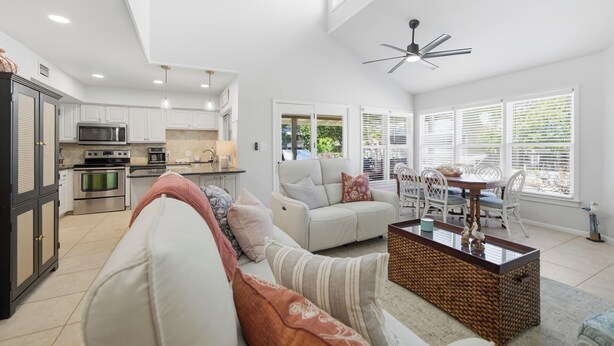 A spacious living area with a sofa, coffee table, and dining table. A kitchen with modern appliances is visible in the background. - Family-Friendly 4BR Cottage with Pool View - Hidden Dunes Resort (Miramar Beach)