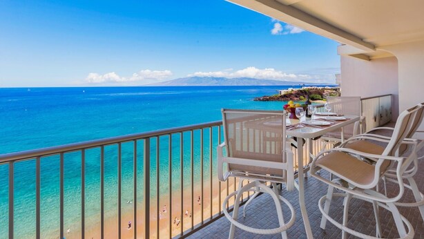 Een balkon met een eettafel, met uitzicht op een strand en de oceaan.