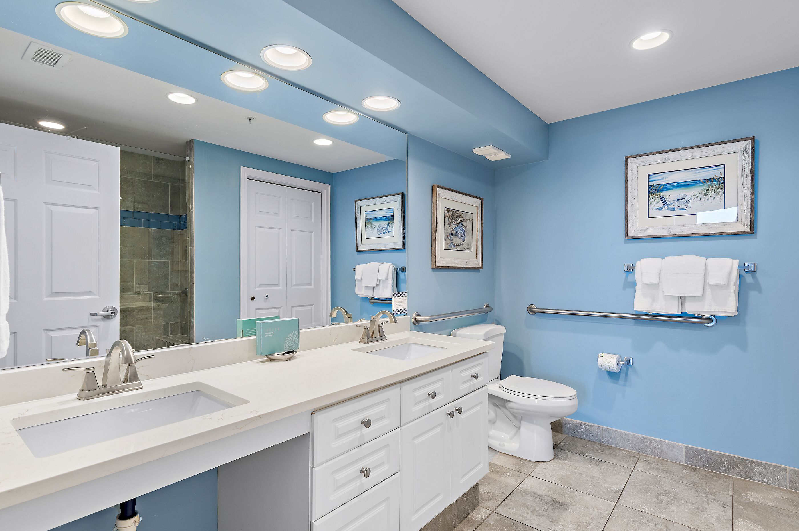 Une salle de bain avec un lavabo blanc, des toilettes, une douche et une barre d’appui.