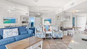 A modern living room with a blue sofa, matching armchairs, a wooden coffee table, and a TV displaying a scenic view. - Gulf Front ~ Private Balcony ~ Pool (Miramar Beach)