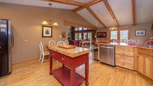 Un'ampia cucina con travi in legno, un'area pranzo con sedie bianche e una lavastoviglie integrata.