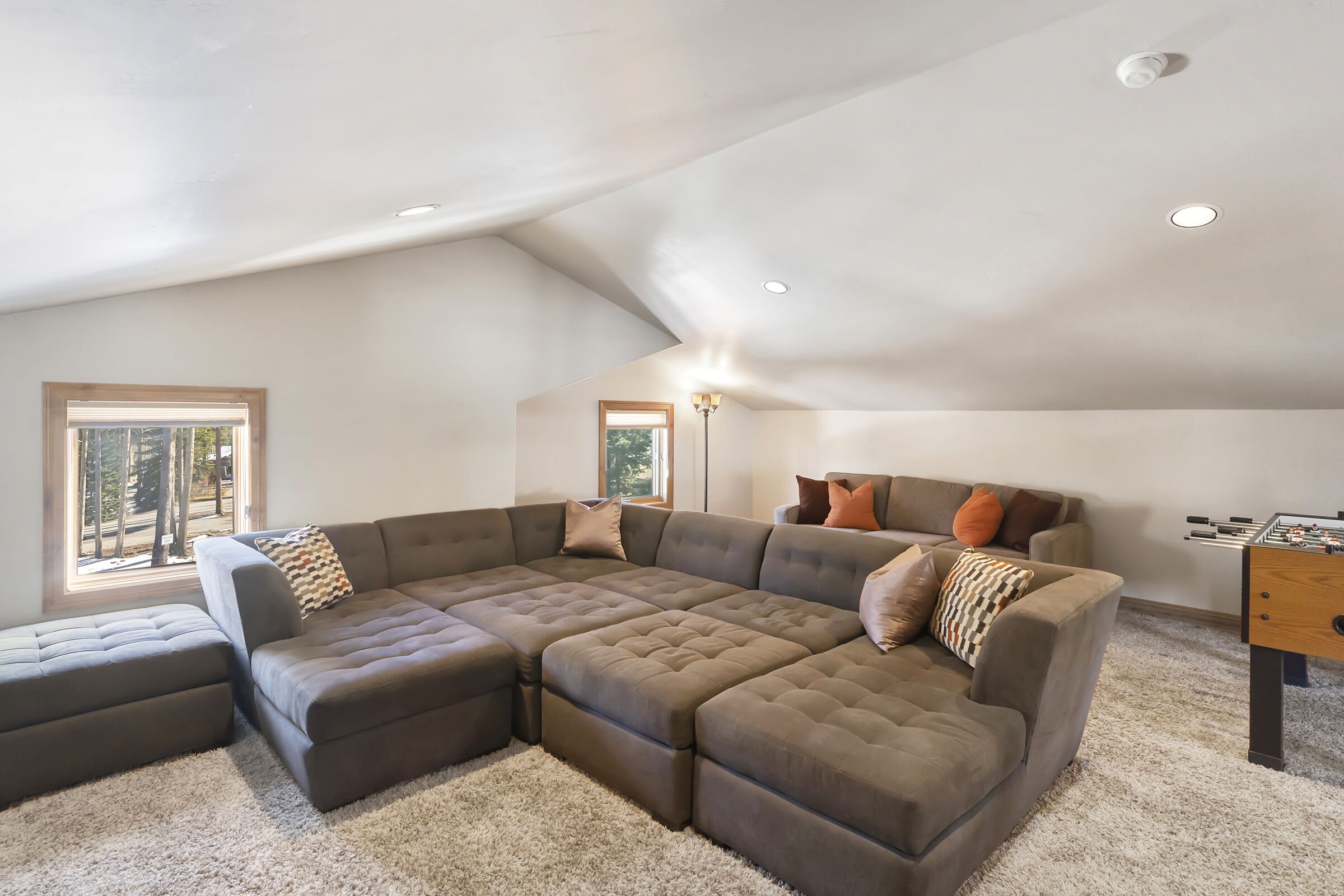 A spacious living room with a sectional sofa, a foosball table, and a large window providing natural light.