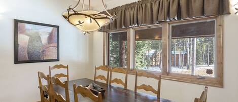 A dining area with a wooden table and chairs, a chandelier, a window with curtains, and a framed picture on the wall.