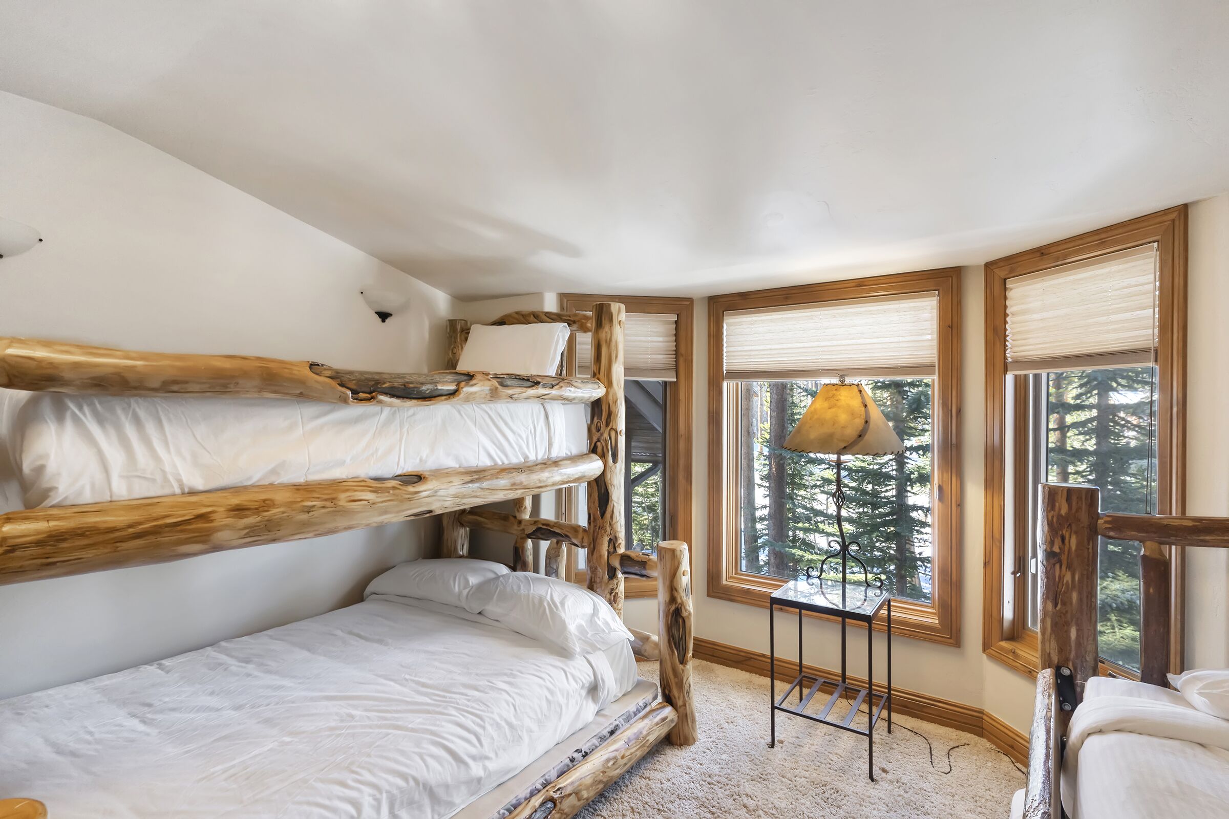 A bunk bed room with a view of trees through large windows.