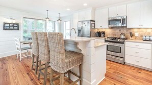 A modern kitchen with white cabinets, stainless steel appliances, and a bar area with wicker chairs.