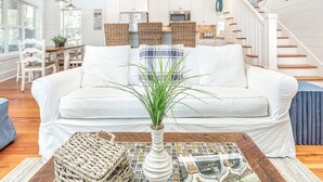 A modern living room with a white sofa, a coffee table with a vase and magazine, and a staircase with fish wall art.