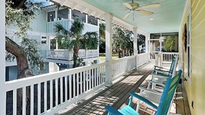 A covered porch with white railings, blue chairs, and a ceiling fan.