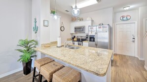 A modern kitchen with granite countertops, stainless steel appliances, and a hanging light fixture. - Coastal Retreat W/ Pool Views, Private Balconies and Spacious Living (Corpus Christi)