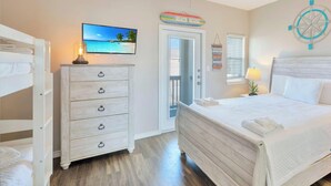A bedroom with a bed, a dresser, a television, a ceiling fan, a window with blinds, and a wall clock. - Coastal Retreat W/ Pool Views, Private Balconies and Spacious Living (Corpus Christi)