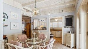 A dining area with wicker chairs and a glass table, a kitchen with white cabinets, and a large mirror above the counter. - 15 Bittern Street | Cozy Home with Cottage & Pool | 4th Row | STR #028425 (Hilton Head Island)