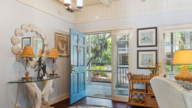 A room with a glass console table, a blue door leading outside, wicker furniture, and framed artwork on the walls. - 15 Bittern Street | Cozy Home with Cottage & Pool | 4th Row | STR #028425 (Hilton Head Island)