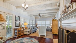 A spacious living room with a fireplace, a ceiling fan, and a large window with blinds. - 15 Bittern Street | Cozy Home with Cottage & Pool | 4th Row | STR #028425 (Hilton Head Island)