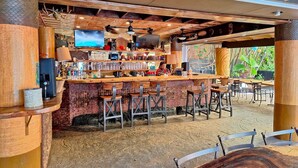 A rustic bar area with wooden furniture, a TV screen, and a view of greenery outside. - Bamboo Hotel - Privately owned Queen Studio - Balcony, Steps to Waikiki Beach (Waikiki)