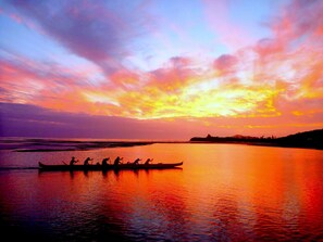 Ein Sonnenuntergang über ruhigem Wasser, ein Tretboot mit Personen.