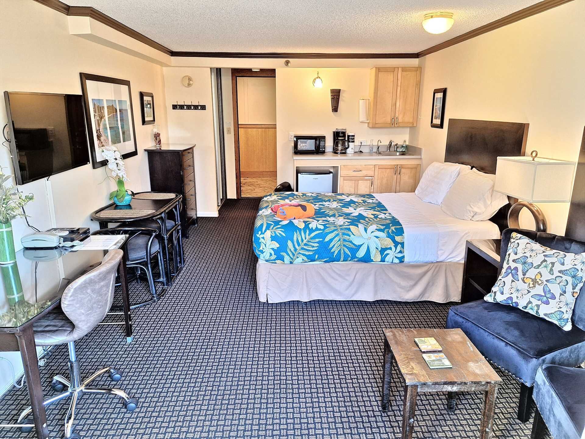 Quarto de hotel com cama, escrivaninha, cadeira, sofá, mesa de centro, micro-ondas, pia e pequena cozinha.