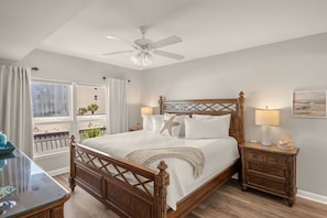 A bedroom with a wooden bed, two bedside tables, a ceiling fan, and a view of the outside.