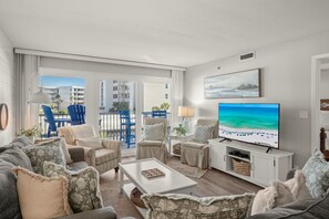 A modern living room with a large flat-screen TV, comfortable seating, and a view of the outdoors.