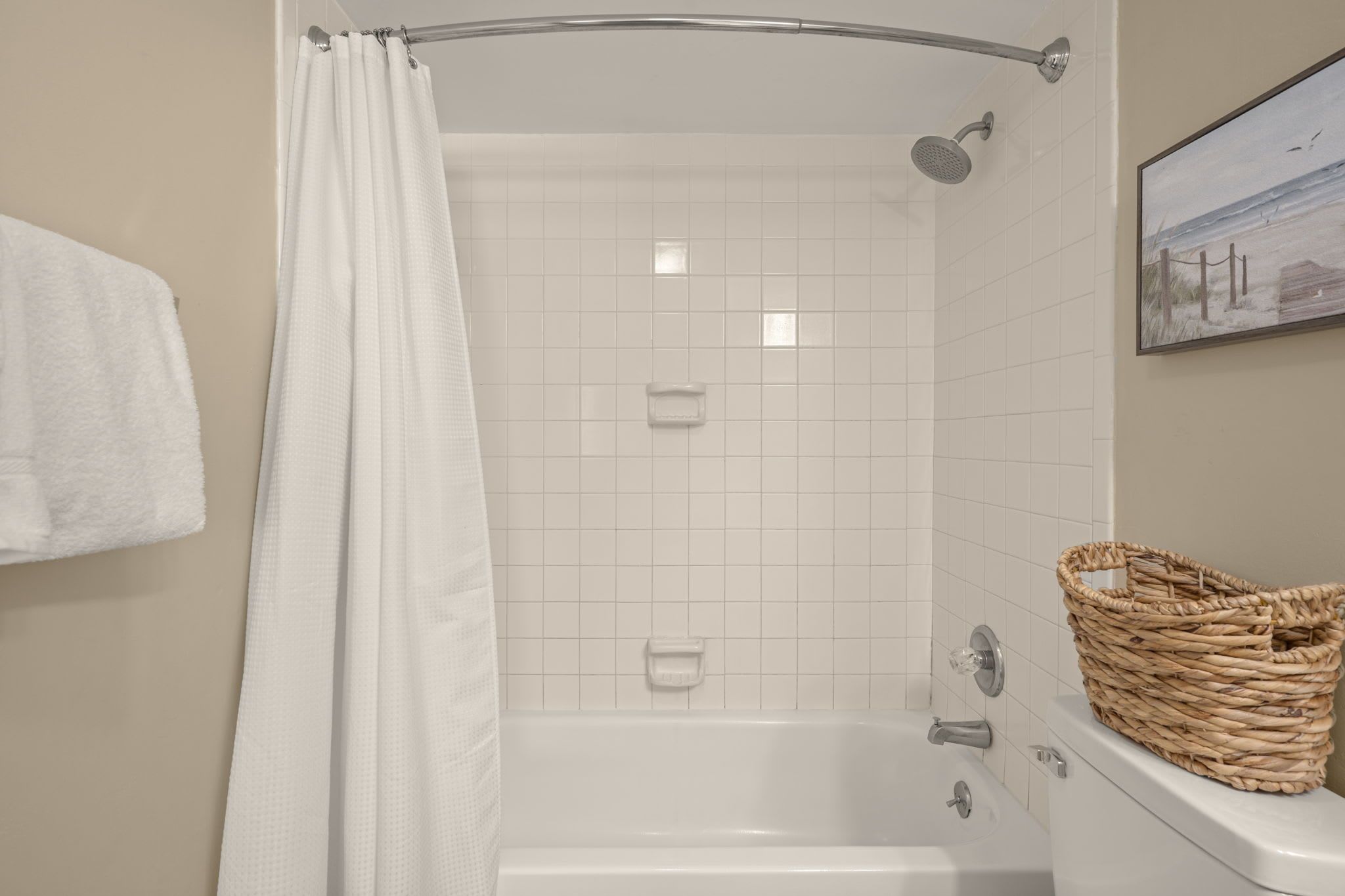 Une douche avec un rideau blanc, une baignoire blanche, une serviette blanche et un panier en osier posé sur le bord.
