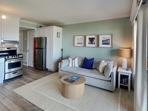 A modern kitchen with stainless steel appliances, a dining area with a round table, and a living room with a sofa and wall art.
